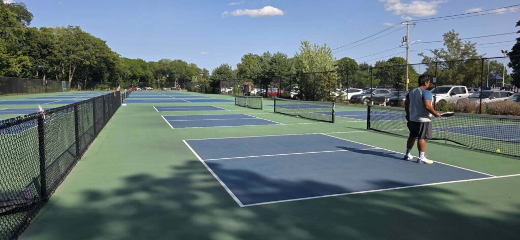 Five outdoor pickleball courts at Doyle Field in Leominster, Massachusetts, with a player at the net on a sunny day