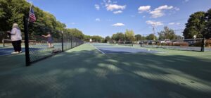 Players during open play on the outdoor pickleball courts at Doyle Field in Leominster, Massachusetts, with an American flag on the fence