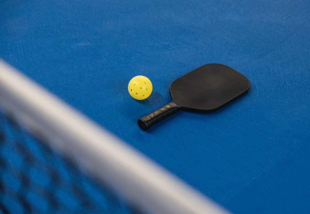 A pickleball paddle, ball and net on a blue court, like the dedicated pickleball courts in Brunswick, Maine
