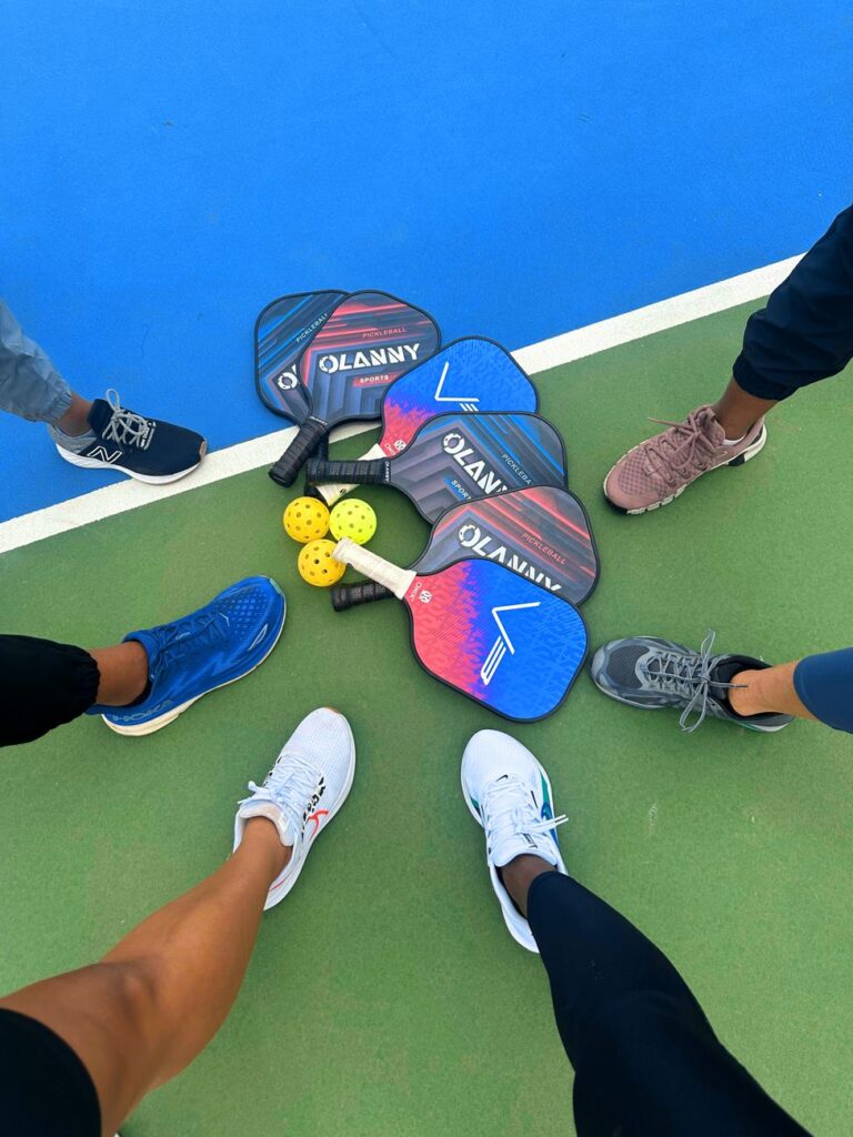 Six pickleball players circle their paddles and balls on court before a sanctioned tournament