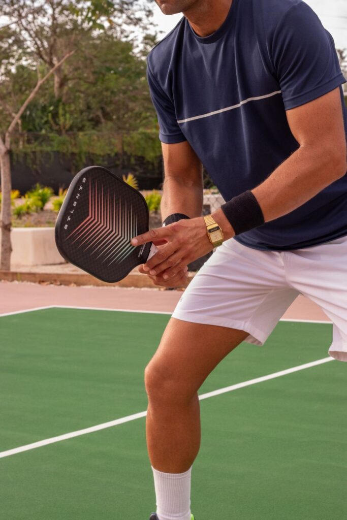 A player in ready position with a paddle at the kitchen line on an outdoor pickleball court