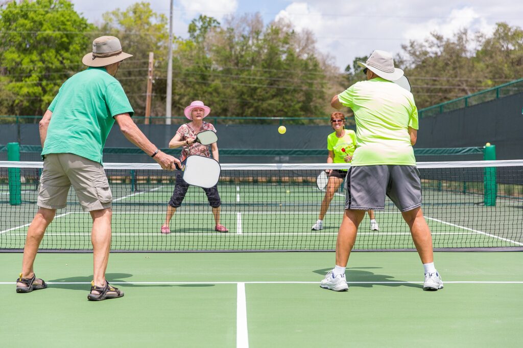 Four pickleball players at the kitchen line in a doubles exchange, the situation where a disguised two-handed backhand decides points