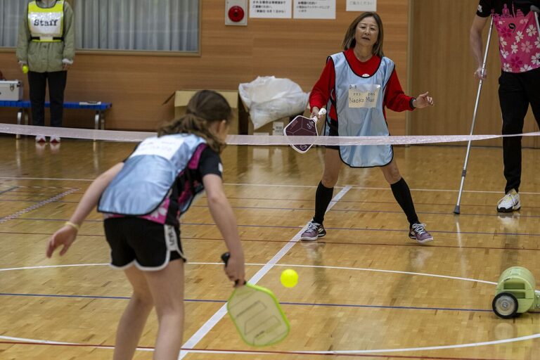 A young player returns a ball on a gym court with a portable net, the kind of setup behind high school pickleball in Massachusetts