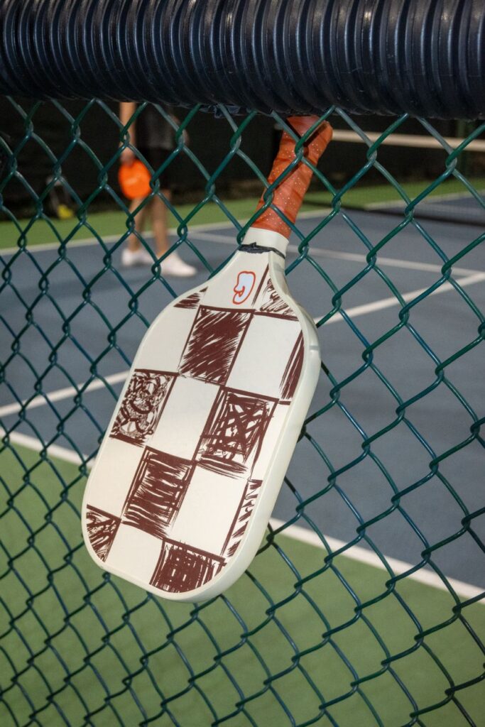 Pickleball paddle hanging on a court fence, showing the paddle face angle that decides a backhand flick in pickleball