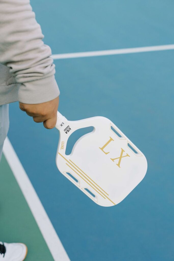 Close-up of a hand holding a pickleball paddle on an outdoor court