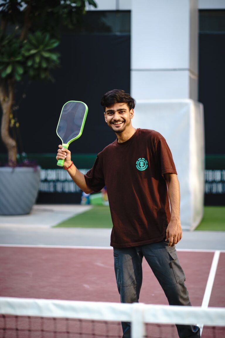 Smiling player holding a paddle behind the net, the social side of pickleball in Marblehead MA