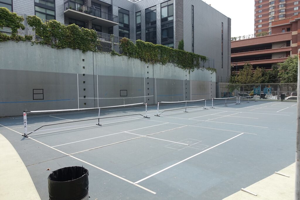 A row of pickleball courts with portable nets set up in an urban park