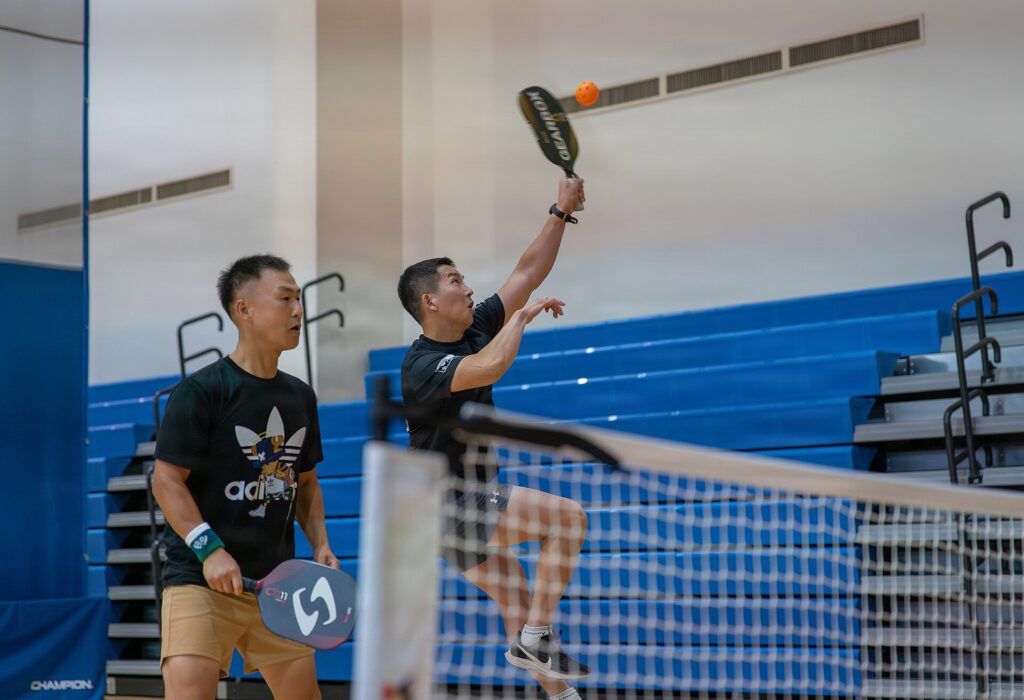 A player reaching high for an overhead at the net in a doubles match, illustrating PPA Tour Europe Barcelona Open results