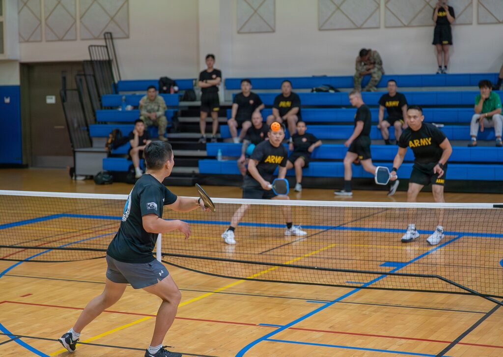 Doubles pickleball players at the kitchen line during an indoor rally, the reset-and-dink game Collin Johns is known for