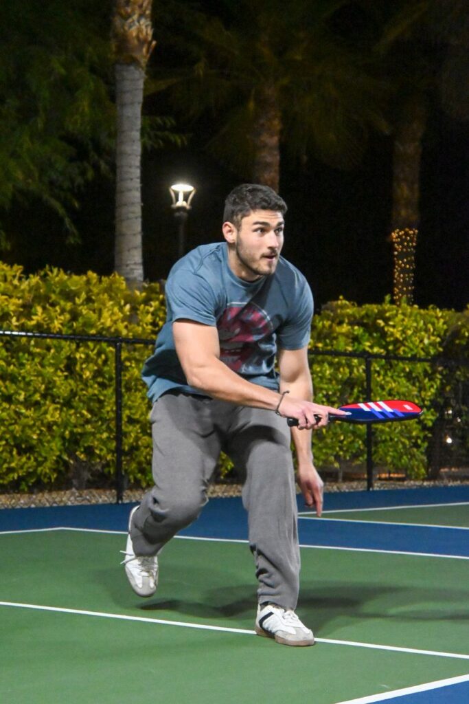 Player mid-swing on an outdoor court at night, the evening play that drives demand for quiet pickleball balls