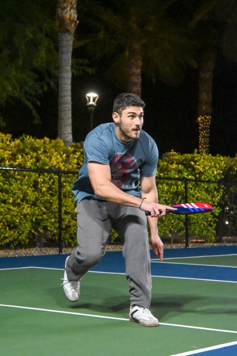 Player mid-swing on an outdoor court at night, the evening play that drives demand for quiet pickleball balls