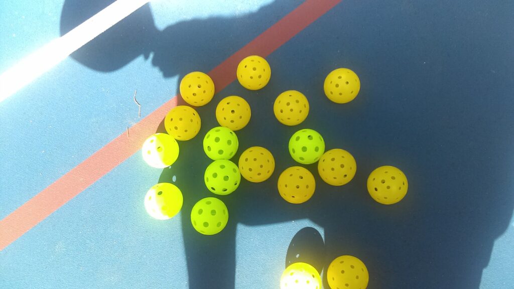 Yellow and green pickleballs scattered on a blue outdoor court, the kind of play where 13mm pickleball paddles once dominated