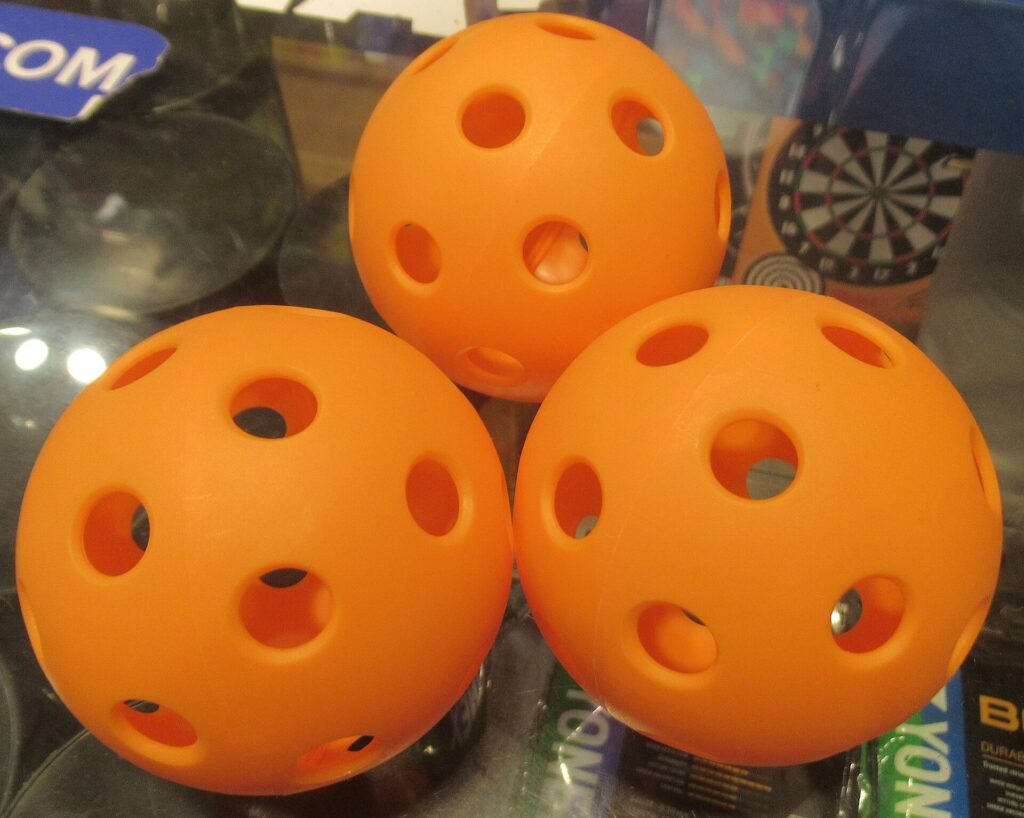 Three orange pickleballs in a sporting goods store display case