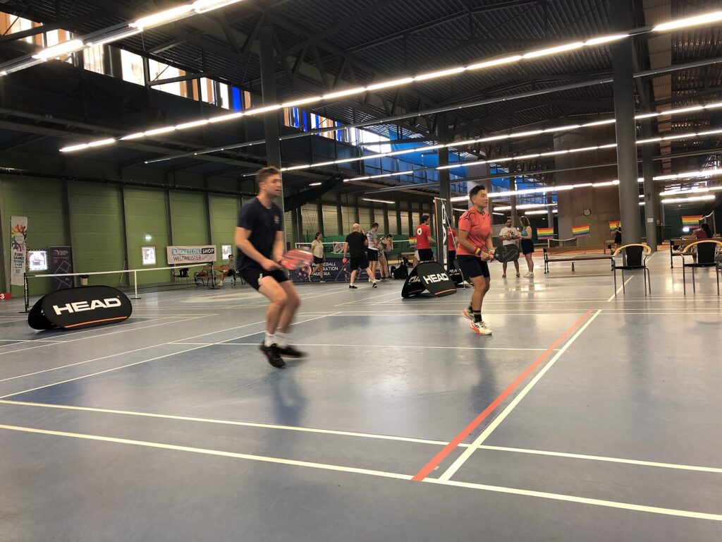 Doubles players on one of several adjacent indoor pickleball courts in a sports hall