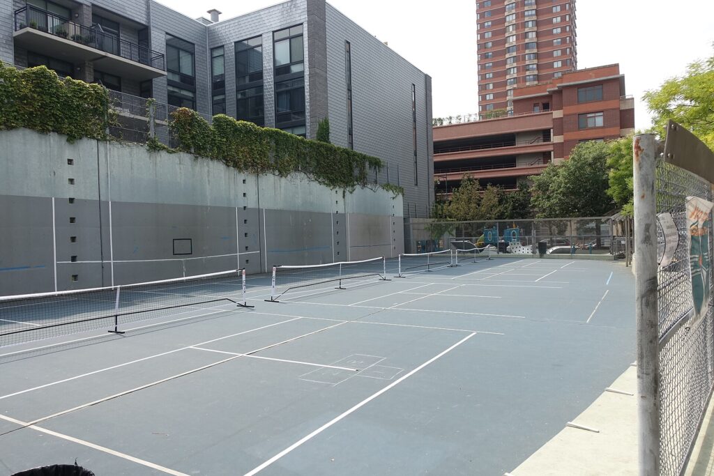 Side-by-side outdoor pickleball courts with portable nets and no dividers, where a stray ball can cause a hinder in pickleball