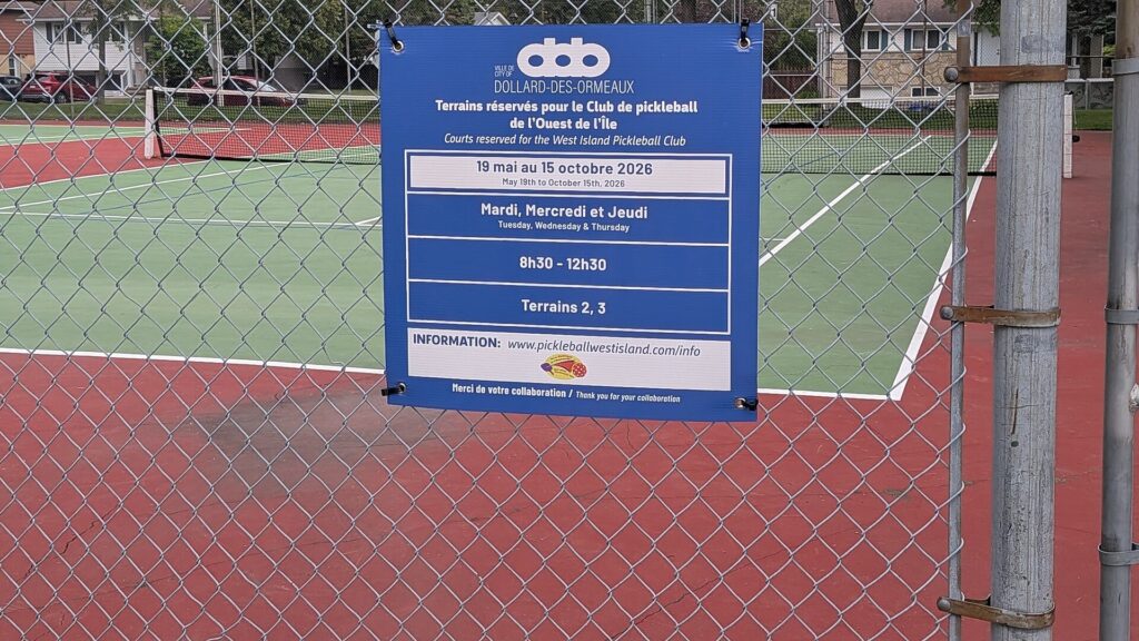 Sign on a chain-link fence reserving public courts for a pickleball club, with houses behind the courts