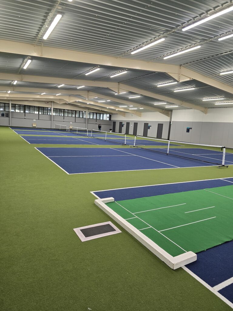 Empty indoor pickleball club with blue courts and portable nets under a steel roof