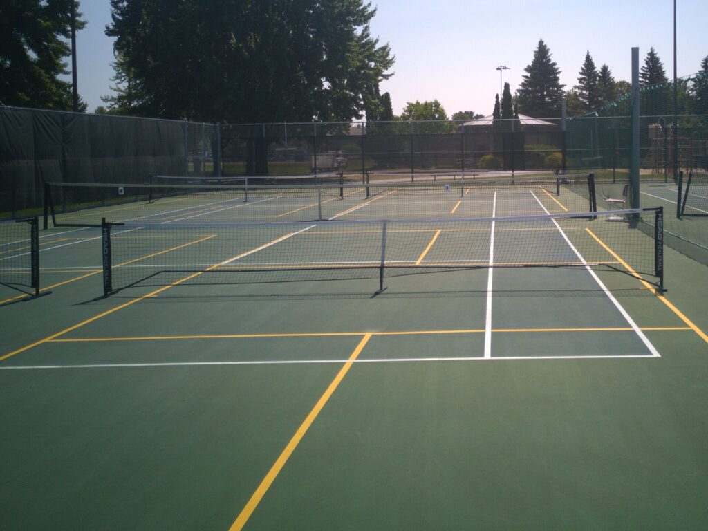 Outdoor pickleball courts with portable nets, fencing and evergreen trees on a sunny day