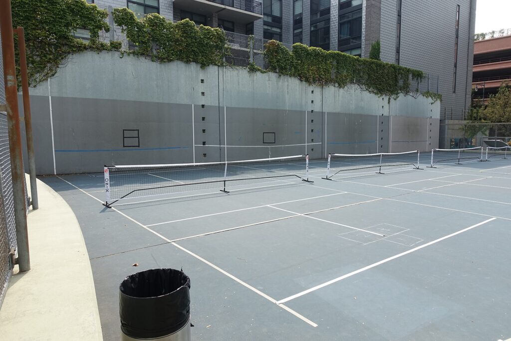 Several pickleball courts with portable nets set up side by side in a public park, where noise from the next court is a hinder rather than a distraction