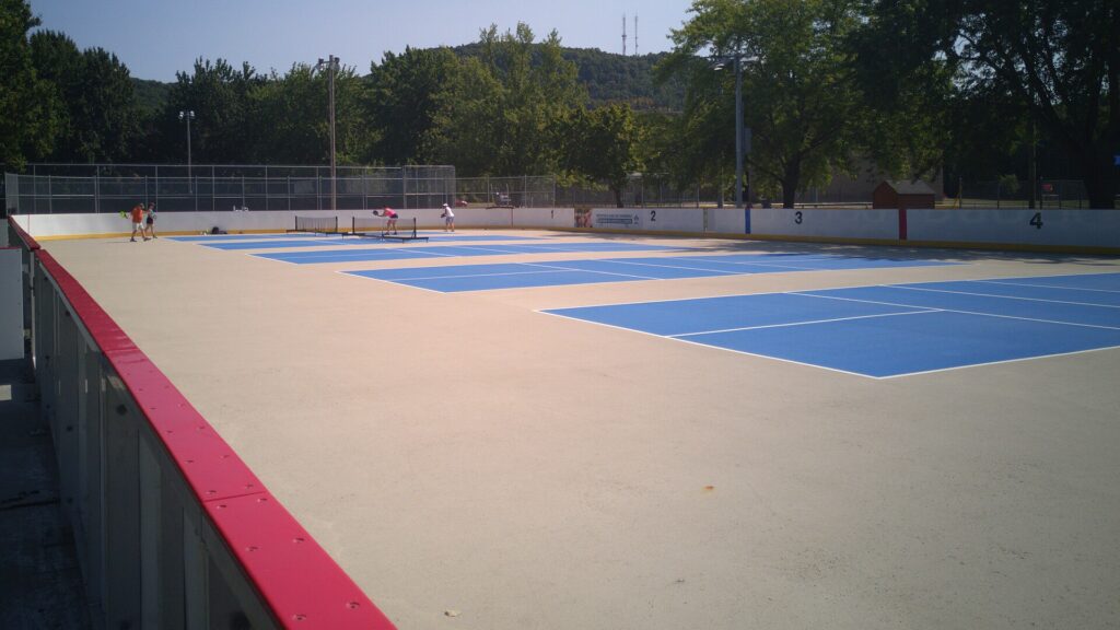 Outdoor courts painted inside a rink with rolling nets, like the town courts for pickleball in Barrington RI