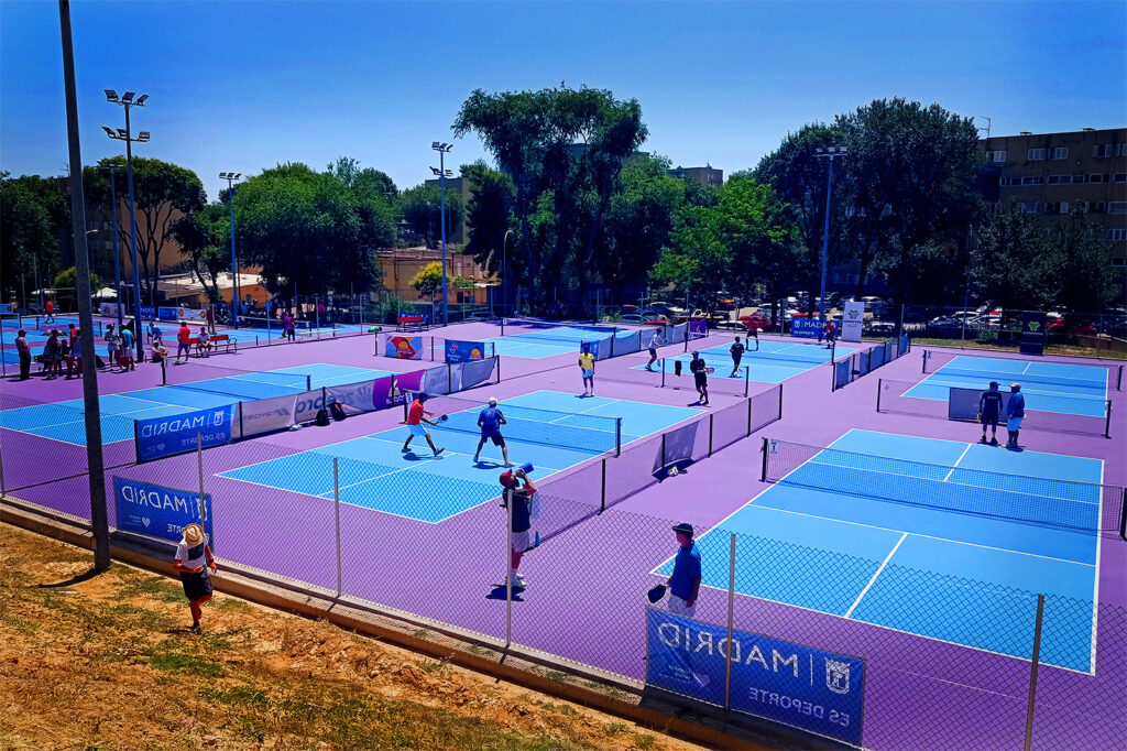 Rows of fenced public outdoor pickleball courts with players in doubles games