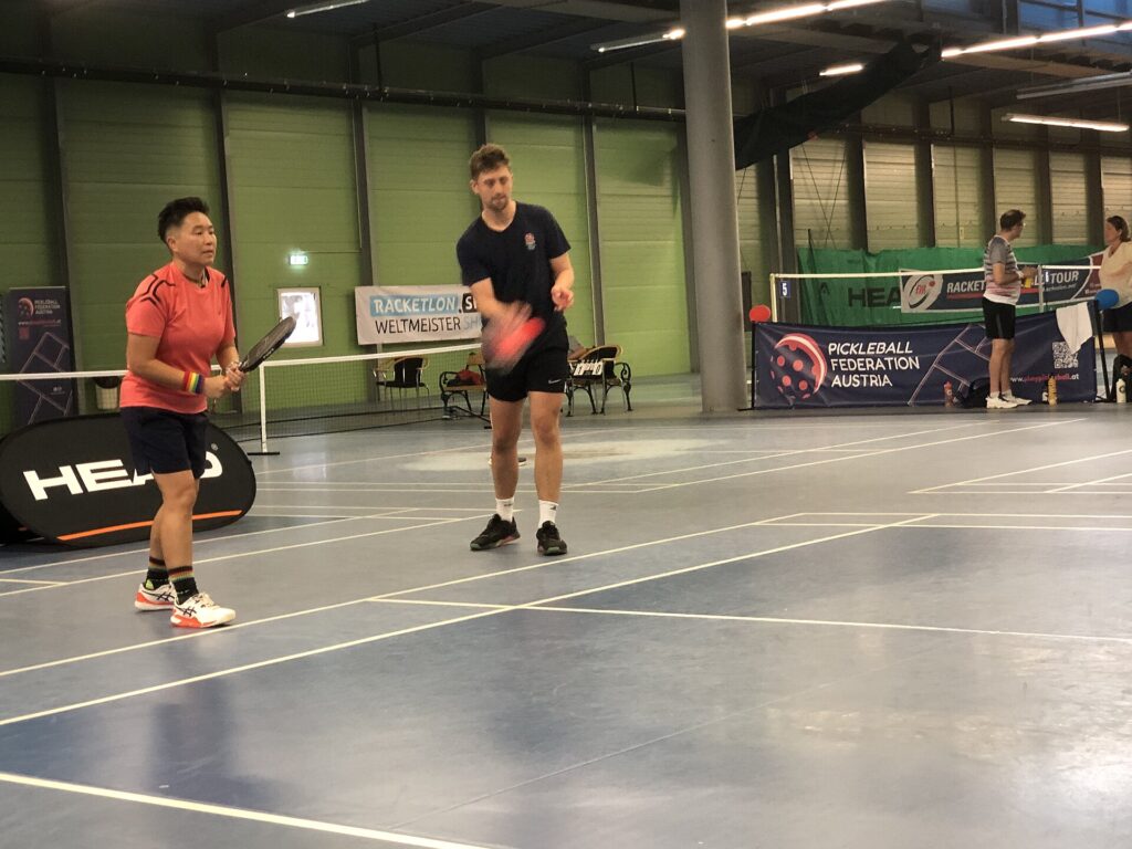 Two doubles partners ready at the baseline on an indoor pickleball court