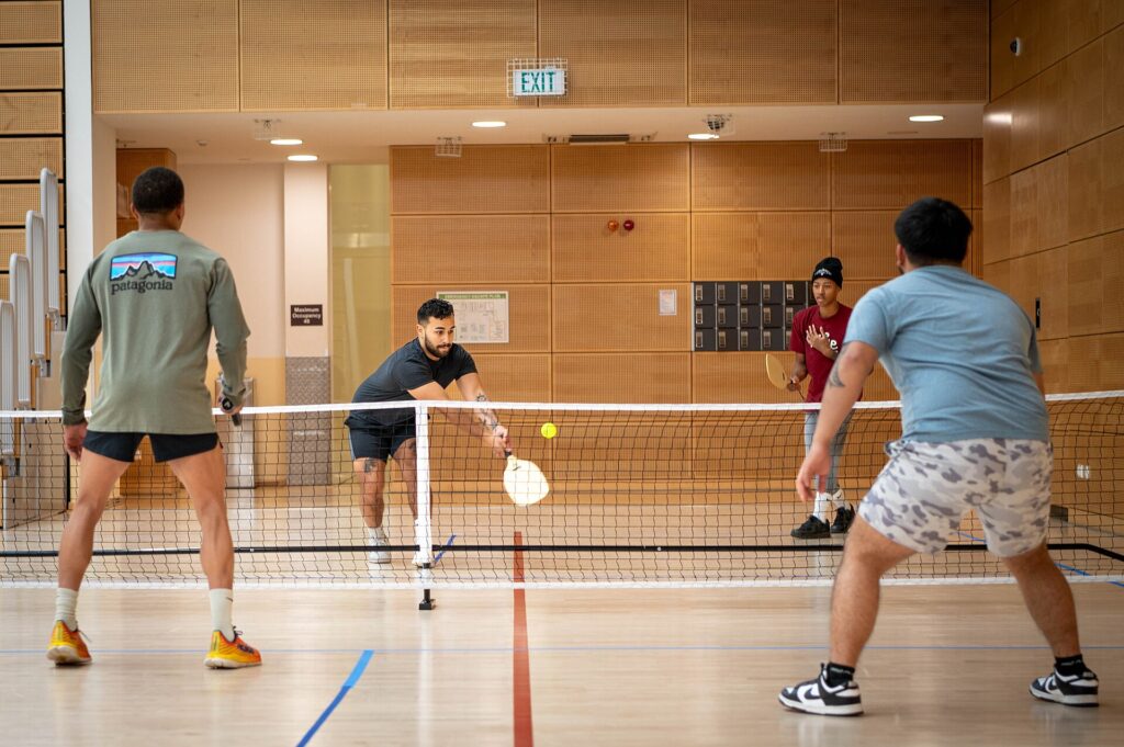 Indoor doubles game on a gym floor with a portable net, illustrating drop-in pickleball in Sanford ME