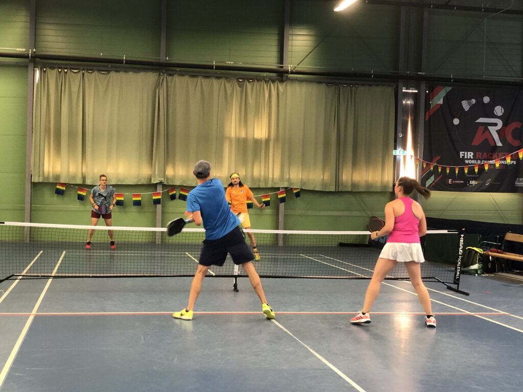 Indoor doubles players at the net swinging paddles of different shapes