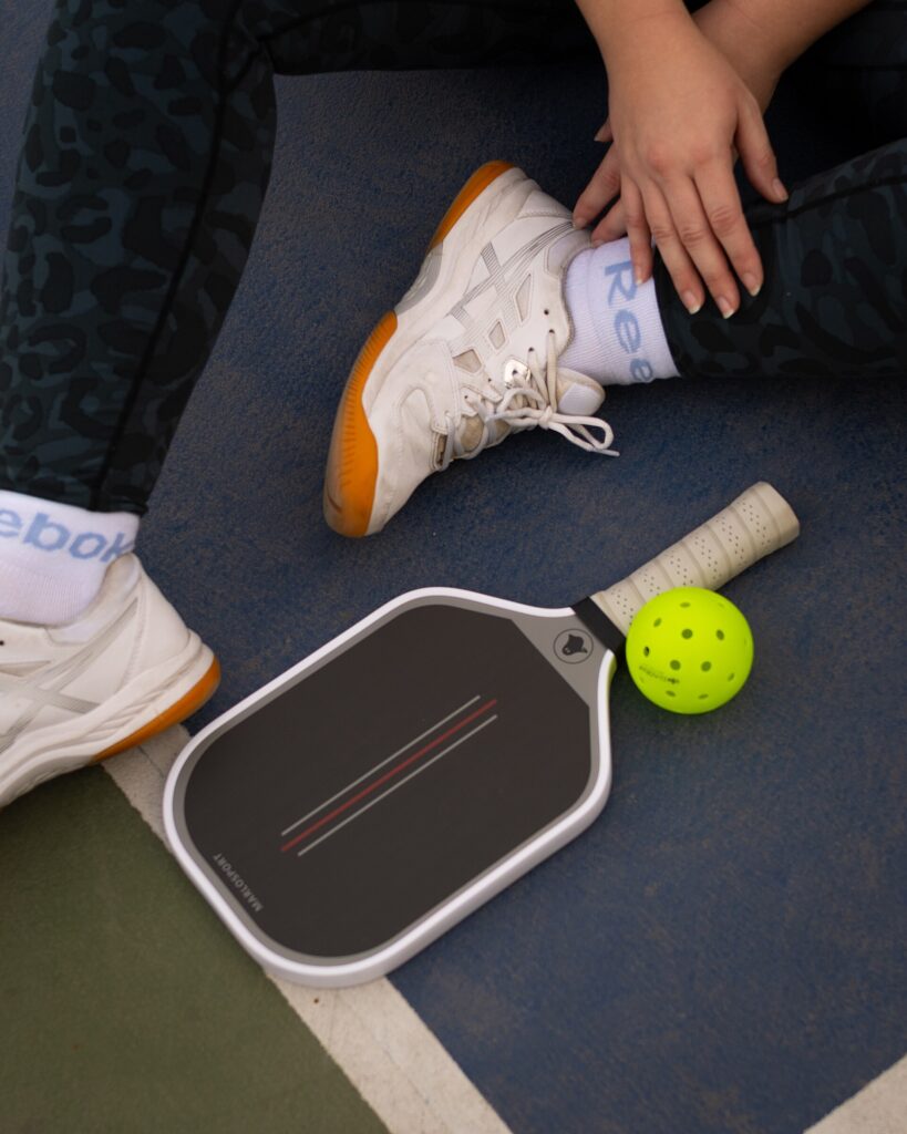 A pickleball paddle and ball on a court, showing the handle-to-head length that sets a pickleball paddle balance point