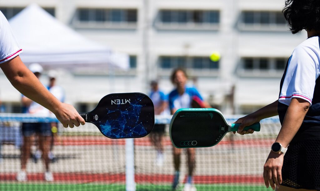 Two players holding paddles of different shapes out over a court, illustrating pickleball paddle swing weight