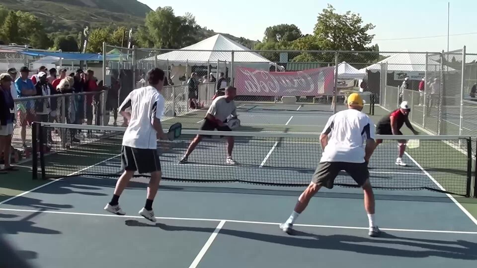 Tournament doubles players at the kitchen line with spectators watching behind the fence