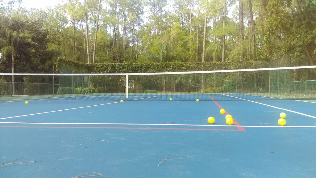 Pickleballs scattered on an outdoor court with painted pickleball lines