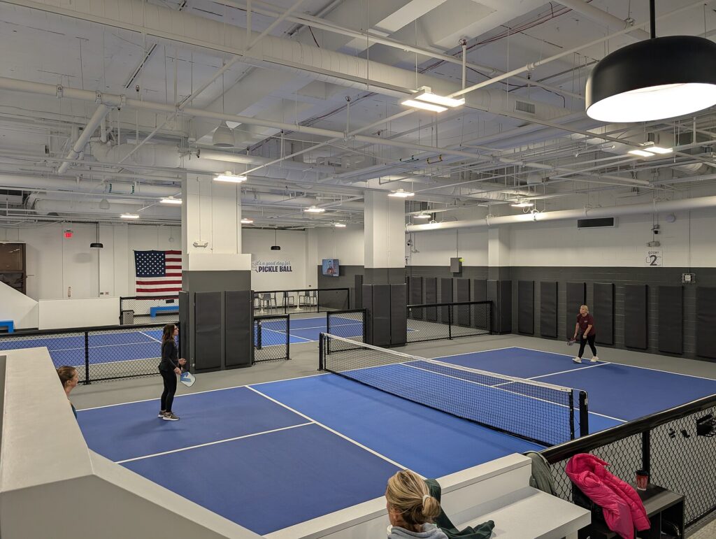Indoor pickleball club courts with players rallying, where fans follow pro pickleball results