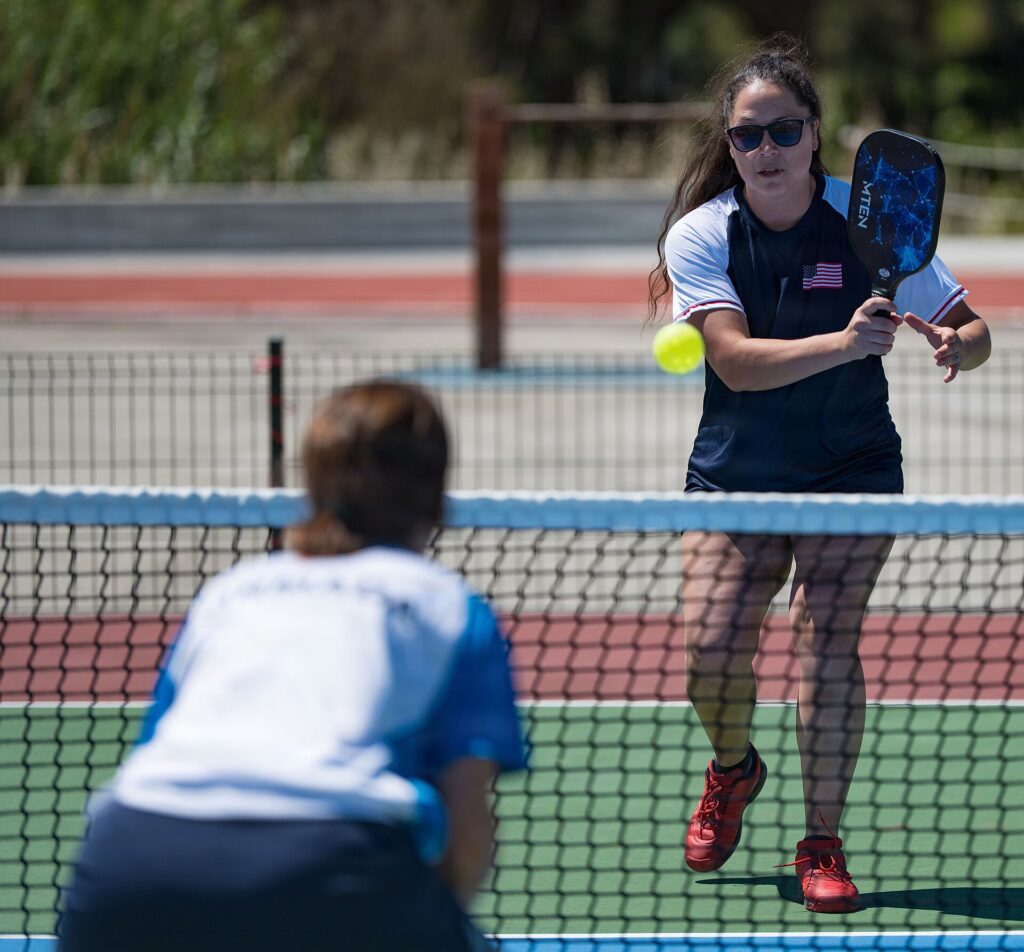Pickleball player hitting a backhand volley at the net with her free hand open beside the paddle