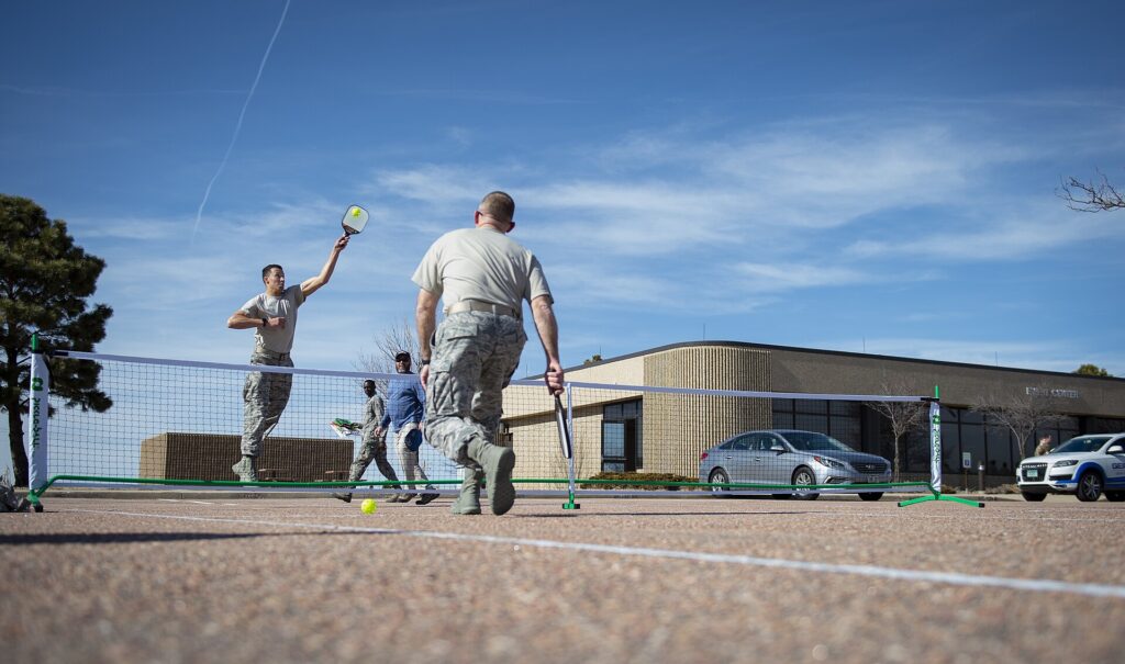 Player stretching high for an overhead on an outdoor pickleball court, a scramble like the get-backs Tyson McGuffin is known for