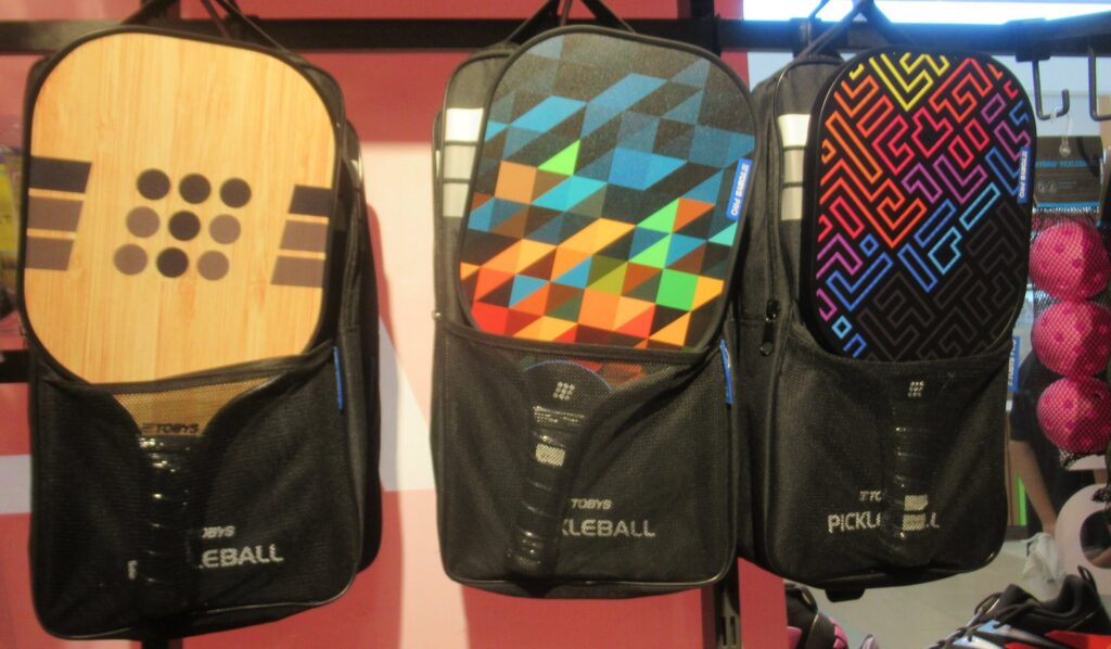 Three pickleball paddles with printed faces hanging in a shop, for a story on Volair HexGrit paddle surfaces